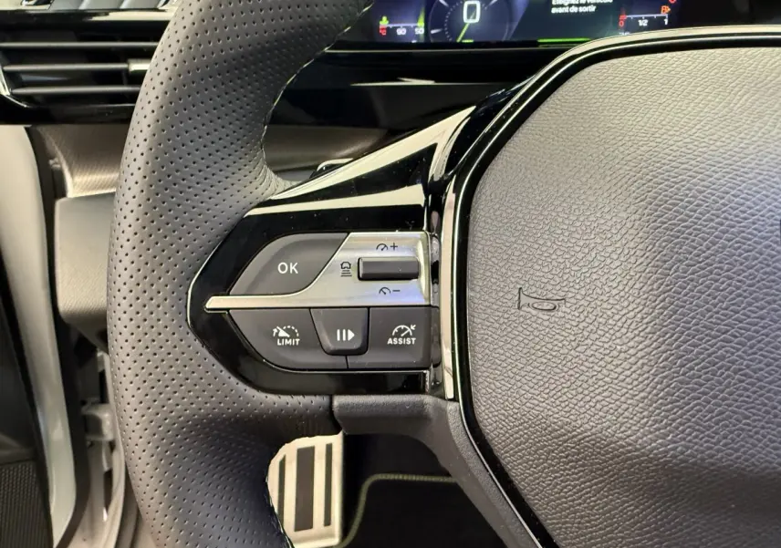 Gros plan sur le volant cuir perforé gauche du Peugeot 308 Hybrid 2024 avec commandes intégrées et tableau de bord digital.