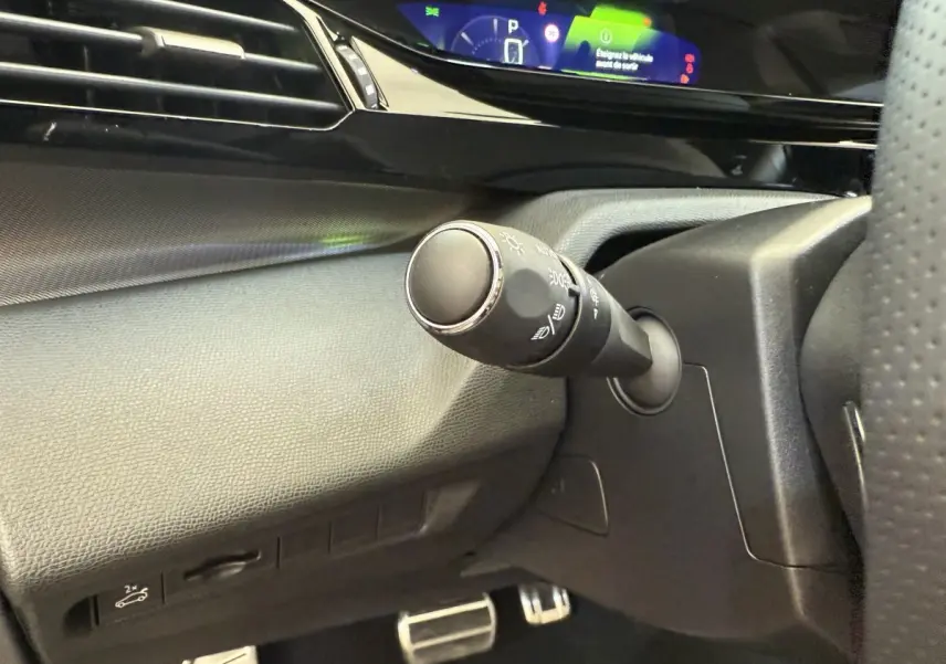 Gros plan sur la commande d'éclairage à gauche du volant dans l'habitacle noir du Peugeot 308 Hybrid 2024.