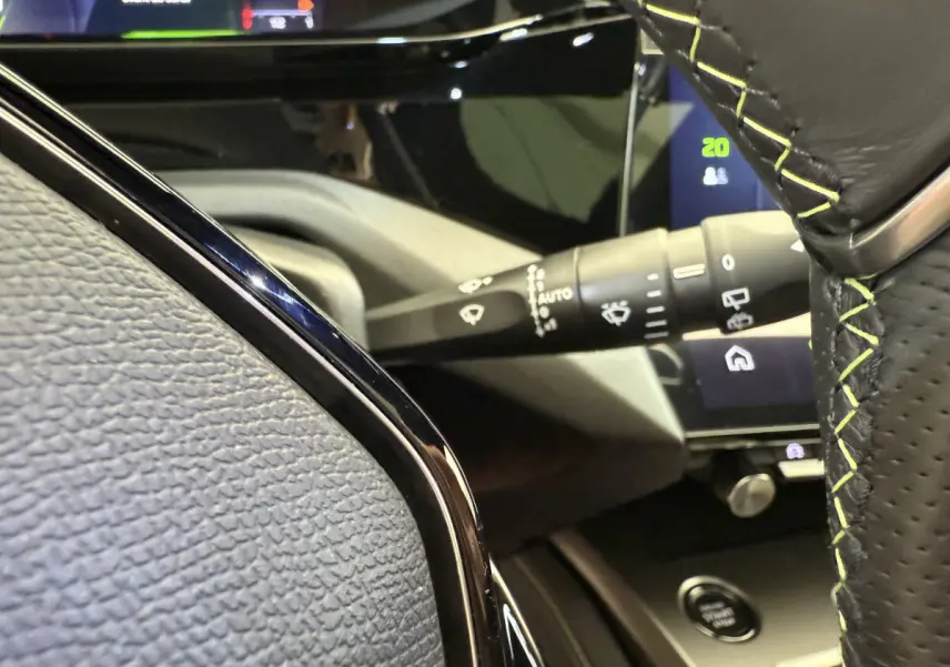 Détail intérieur du volant cuir noir avec surpiqûres vertes et commandes, tableau de bord tactile Peugeot 308 Hybrid 2024.