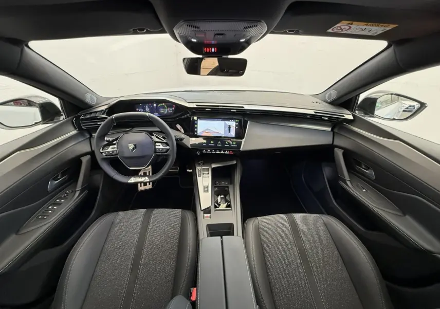 Vue intérieure avant du Peugeot 308 Hybrid 136 e-DCS6 GT 2024, tableau de bord moderne avec écran tactile central et volant cuir.
