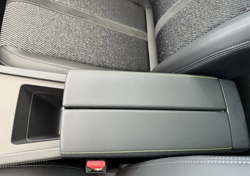 Vue rapprochée de l'accoudoir central noir avec surpiqûres vertes dans l'habitacle de la Peugeot 308 Hybrid 2024.