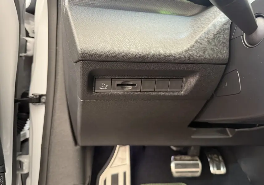 Gros plan sur la commande d'ouverture du coffre côté gauche, intérieur noir, pédales alu visibles, Peugeot 308 blanc 2024.