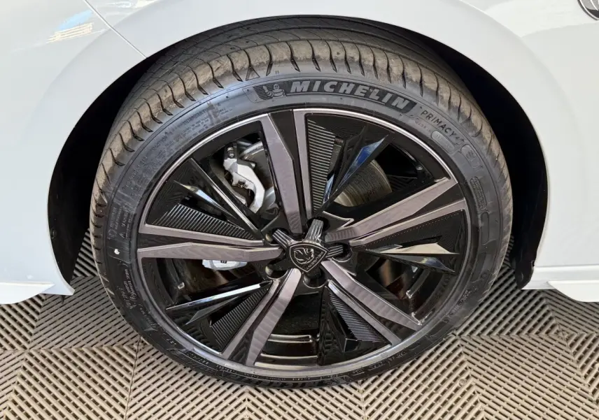 Gros plan sur la roue avant droite de la Peugeot 308 Hybrid 136 e-DCS6 GT blanche avec jante noire brillante et logo lion central.