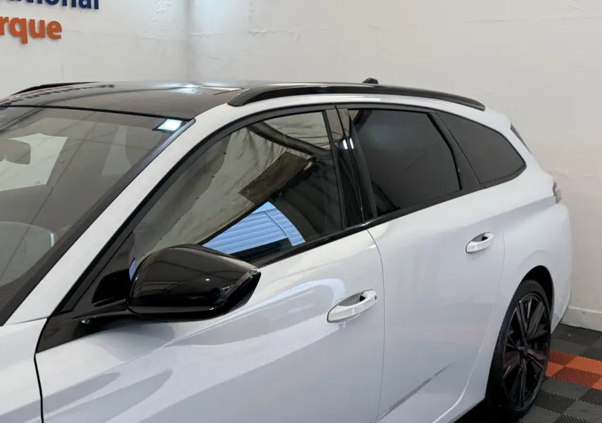 Vue latérale droite d'une Peugeot 308 Hybrid 136 e-DCS6 GT blanche avec toit noir et rétroviseur noir brillant.