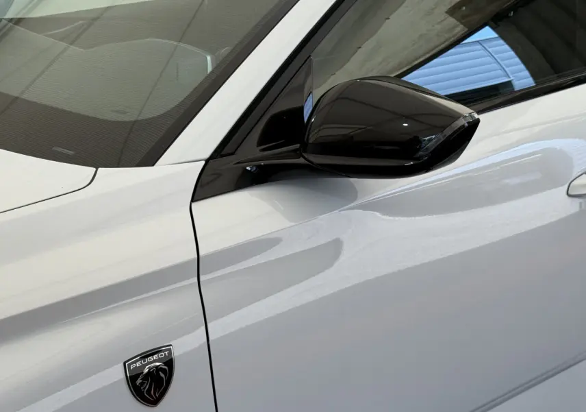Détail du côté gauche blanc d'une Peugeot 308 Hybrid 136 e-DCS6 GT avec rétroviseur noir brillant et logo lion.