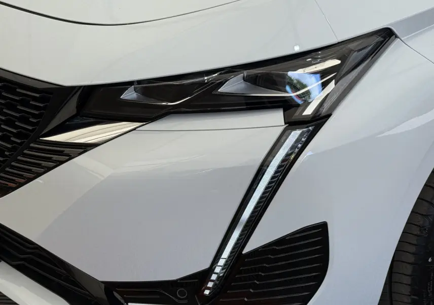 Gros plan sur le phare avant droit blanc de la Peugeot 308 Hybrid 136 e-DCS6 GT avec signature lumineuse LED distinctive.