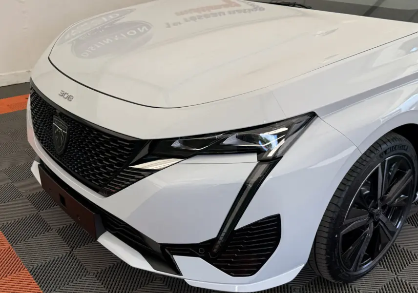 Vue 3/4 avant droit d'une Peugeot 308 Hybrid 136 e-DCS6 GT blanche avec calandre noire et phares LED distinctifs.