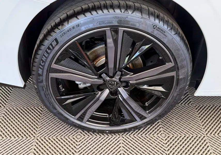 Gros plan sur la roue avant droite noire brillante de la Peugeot 308 Hybrid 136 e-DCS6 GT blanche, pneu Michelin visible.