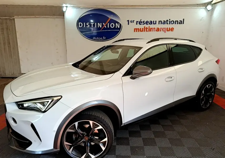 Vue 3/4 avant droite d'un CUPRA Formentor blanc avec jantes noires et détails gris métallisé en intérieur showroom.