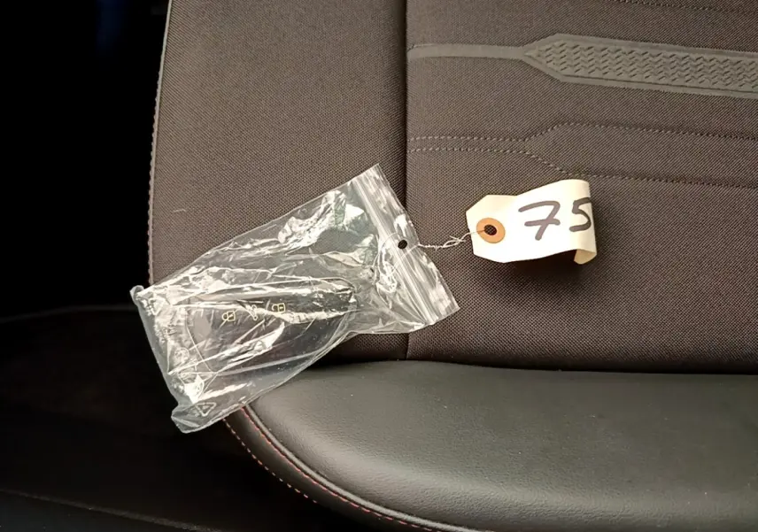 Gros plan sur la clé de contact dans un sachet plastique posée sur un siège tissu gris foncé avec surpiqûres rouges.