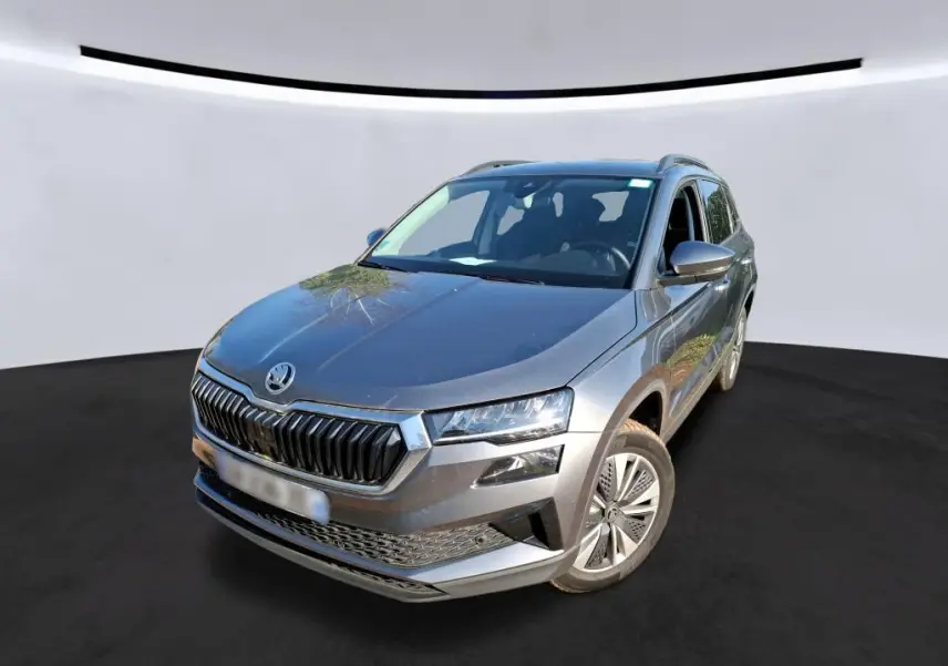 Vue 3/4 avant droite d'un Skoda Karoq gris 2023 avec jantes alu 17'' et calandre chromée, en intérieur showroom.