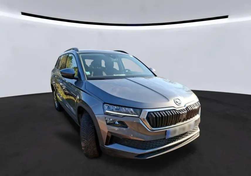Vue frontale d'un Skoda Karoq gris 2023 avec calandre noire et logo chromé, en intérieur showroom.
