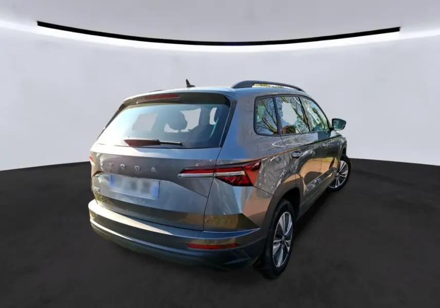 Vue 3/4 avant gauche d’un Skoda Karoq gris métallisé avec calandre chromée et jantes alu 17 pouces en intérieur showroom.