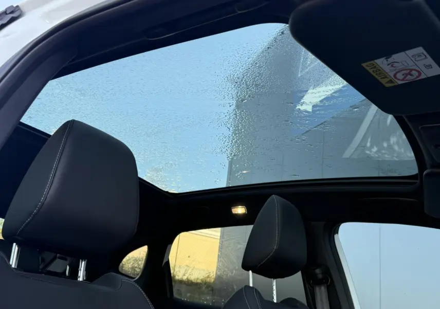 Vue intérieure du toit panoramique en verre du Nissan Qashqai blanc nacré avec sièges avant noirs et ciel de toit noir.