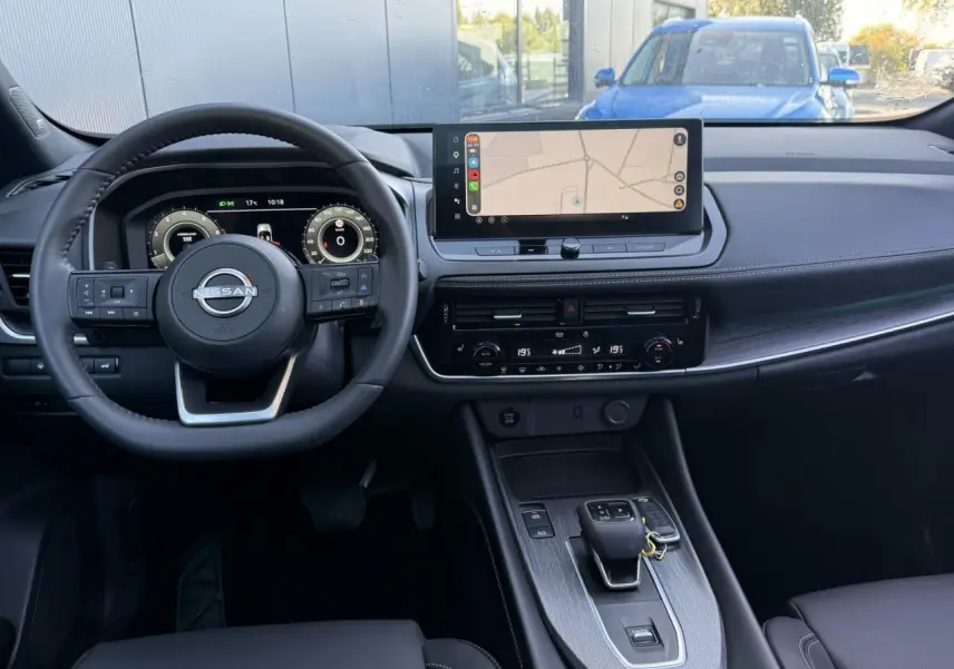 Vue intérieure frontale du tableau de bord du Nissan Qashqai 2025 avec écran tactile GPS et volant cuir noir.