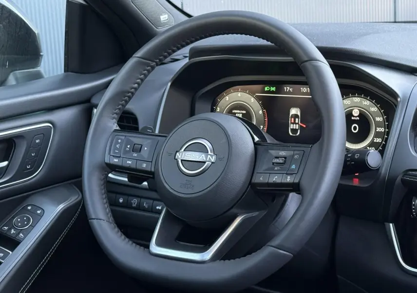 Vue intérieure centrée sur le volant cuir noir du Nissan Qashqai 2025 avec tableau de bord numérique et commandes intégrées.