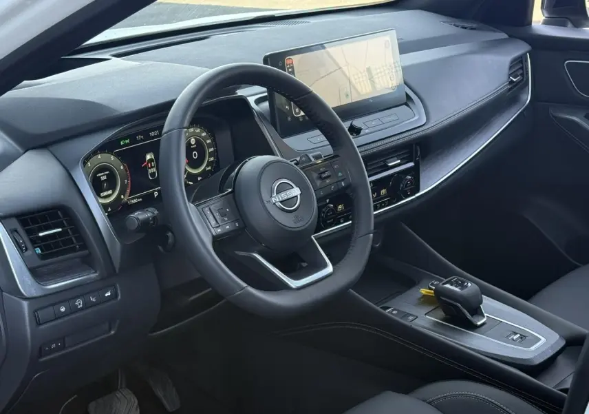 Vue intérieure côté conducteur du tableau de bord noir du Nissan Qashqai 2025 avec écran tactile et volant cuir.