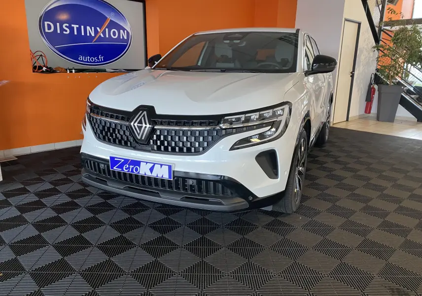 Renault Austral E-Tech 200 Techno blanc nacré vu de face droite en intérieur avec calandre noire à damiers et phares LED distinctifs.