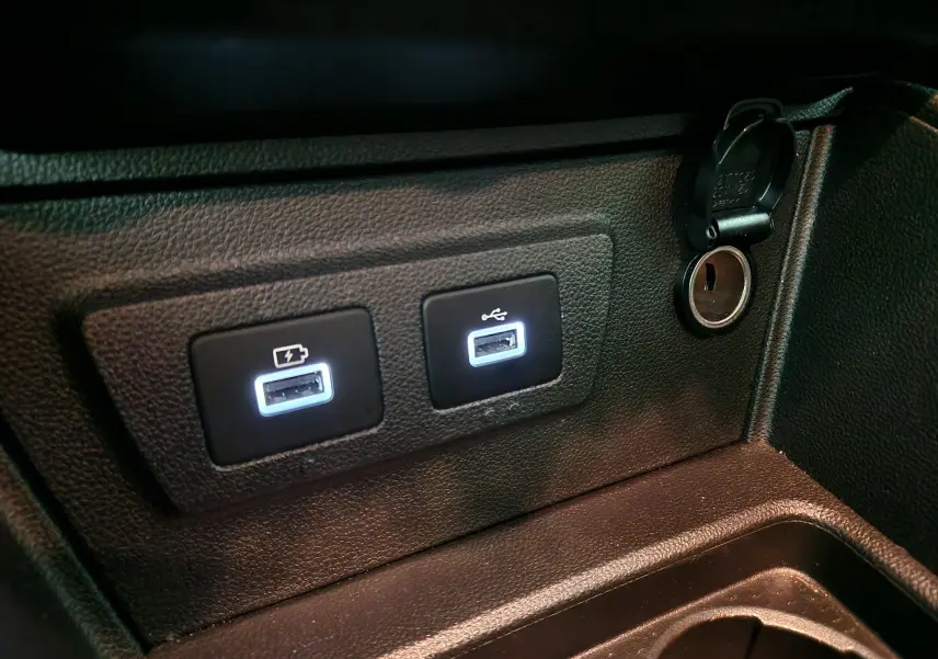 Prise USB double et allume-cigare dans l'habitacle noir du Dacia Duster 4x4 2024, vue rapprochée côté console centrale.