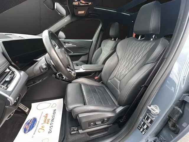 Intérieur BMW X1 2024 en cuir Vernasca noir, vue côté conducteur avec sièges avant électriques et toit panoramique ouvert.