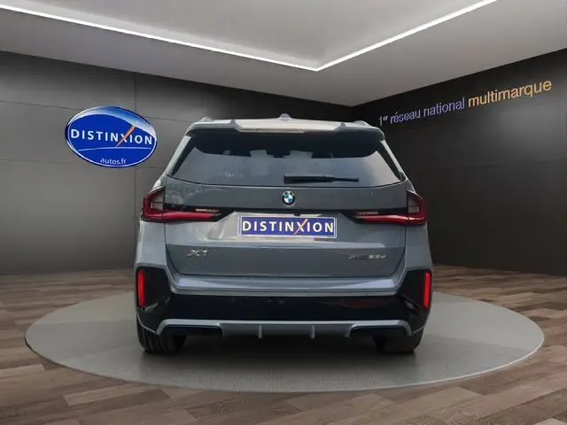 Vue arrière d'un BMW X1 Storm Bay 2024 avec feux LED et détails noirs contrastants dans un showroom.