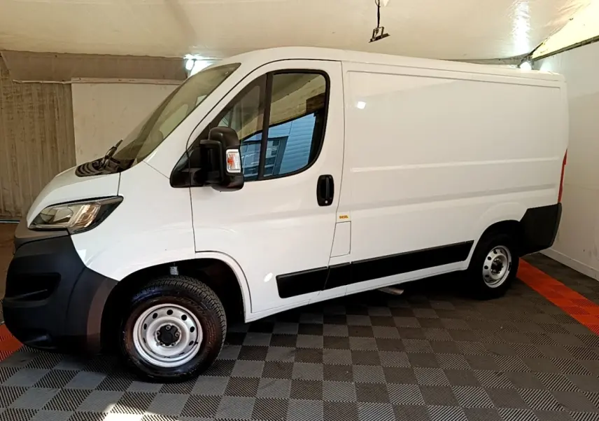 Vue latérale gauche d’un FIAT Ducato Fourgon blanc 2021 avec jantes acier et rétroviseurs noirs dans un garage.