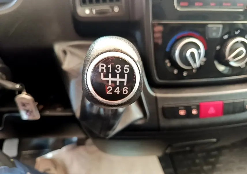 Gros plan sur le levier de vitesses manuel du Fiat Ducato Fourgon blanc, avec tableau de bord et commandes de climatisation en arrière-plan.