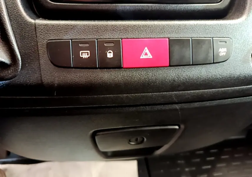 Gros plan sur les boutons de commande noirs et rouge du tableau de bord du Fiat Ducato Fourgon blanc, version 2021.