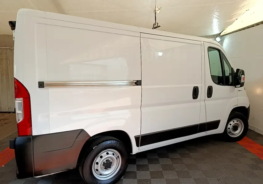 Fiat Ducato Fourgon blanc vu de profil côté droit, avec bande noire sur les bas de caisse et jantes acier.
