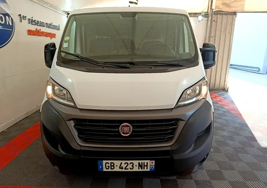 Vue frontale d’un FIAT Ducato Fourgon blanc avec calandre noire et phares allumés dans un garage.