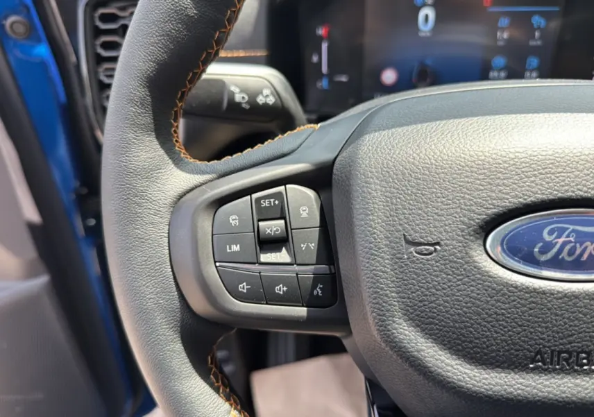 Gros plan sur le volant cuir noir avec surpiqûres marron du Ford Ranger 2025 Bleu Lightning, boutons multifonctions visibles.