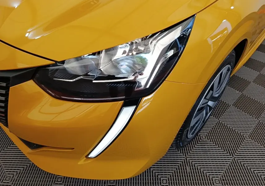 Gros plan sur le phare avant droit et la calandre d'une Peugeot 208 jaune vif, avec feux LED en forme de griffes.