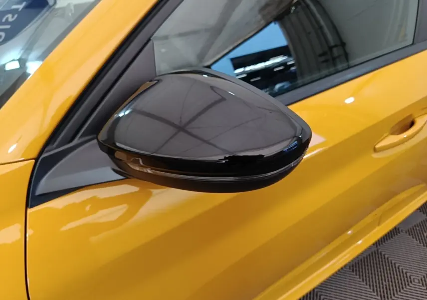 Rétroviseur noir brillant côté gauche d’une Peugeot 208 jaune vue de près, avec poignée de porte visible.