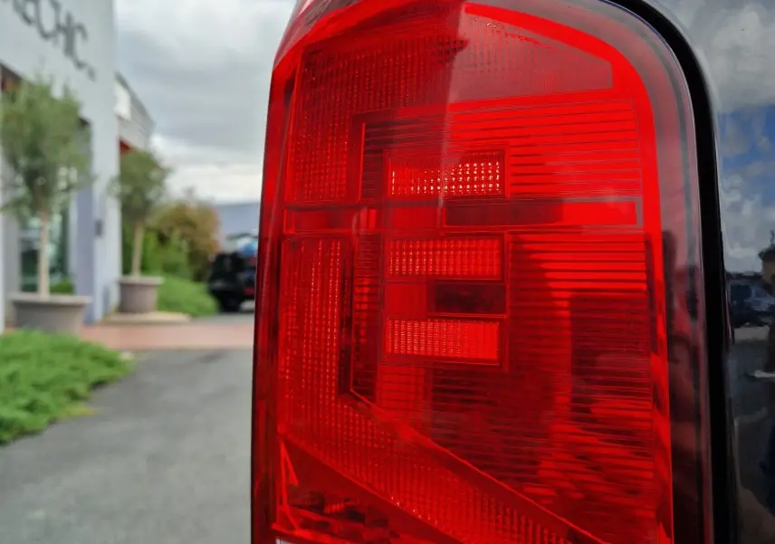 Gros plan sur le feu arrière droit rouge du Volkswagen Transporter noir, reflétant le ciel et un bâtiment en arrière-plan.