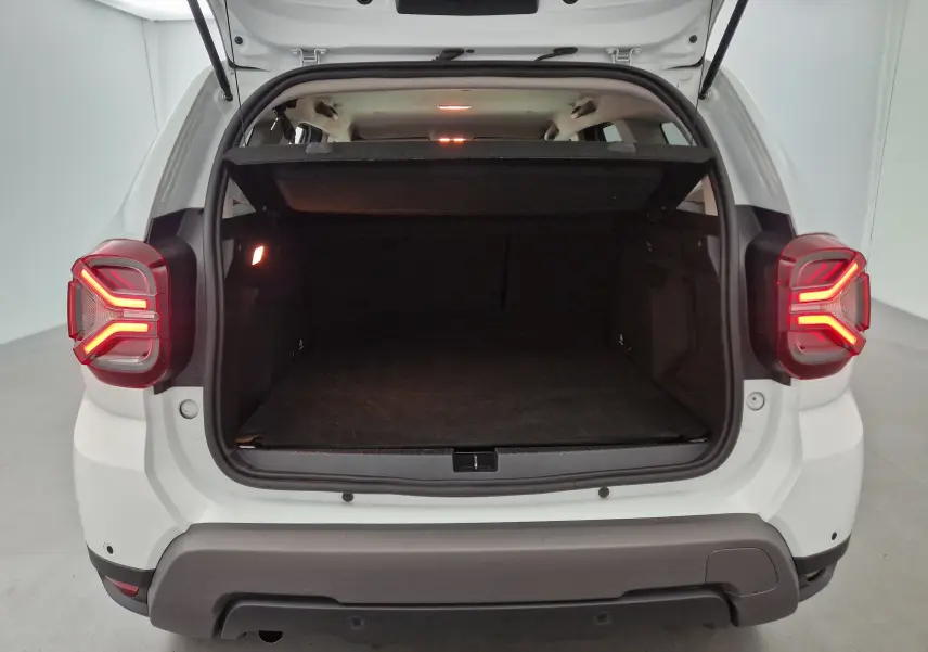 Coffre ouvert vu de l'arrière d'un Dacia Duster blanc 2024 avec feux arrière allumés et intérieur spacieux visible.