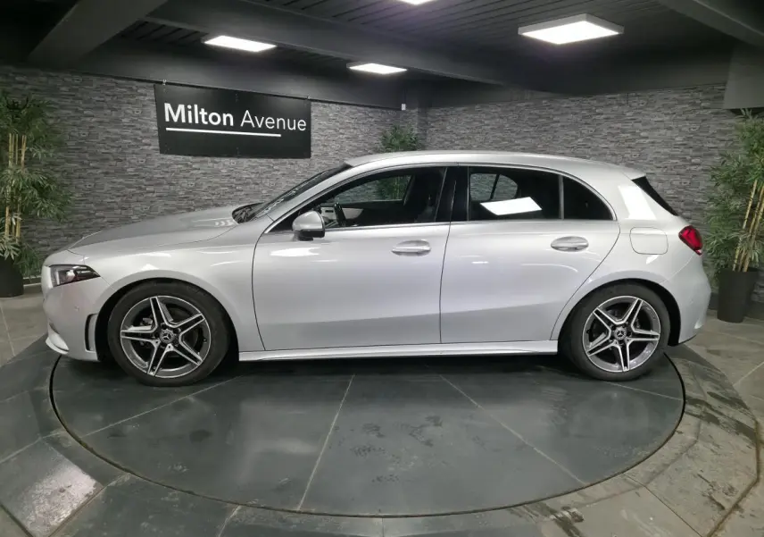 Profil côté gauche d'une Mercedes Classe A 200 d AMG Line gris métallisé avec jantes AMG 18 pouces en intérieur showroom.