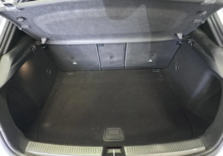 Coffre ouvert vu de l'arrière d'une Mercedes Classe A AMG Line gris, espace de chargement vide et tapis noir.
