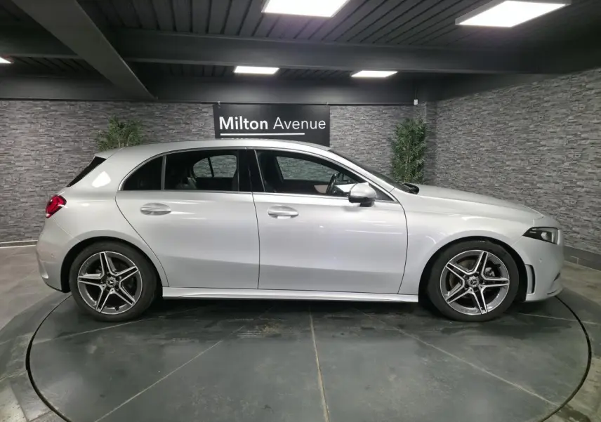 Profil côté gauche d'une Mercedes Classe A gris métallisé AMG Line avec jantes alliage cinq branches dans un showroom.