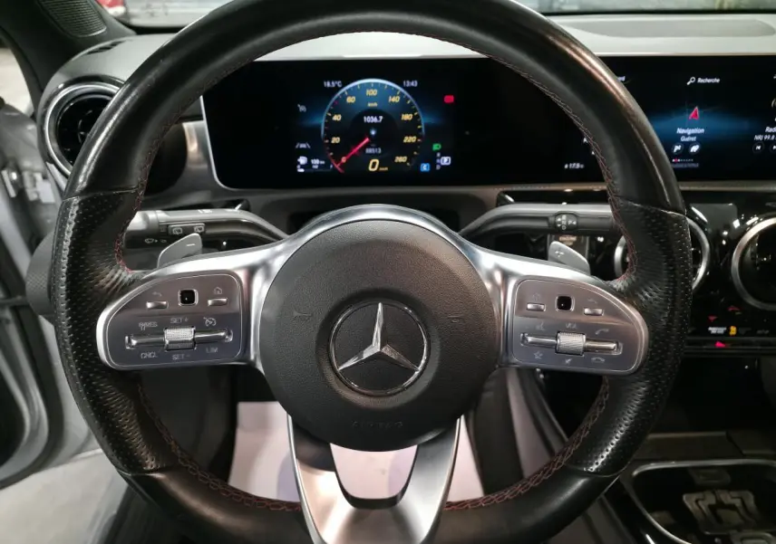 Vue rapprochée du volant sport cuir noir avec surpiqûres rouges et tableau de bord numérique de la Mercedes Classe A AMG Line 2019.