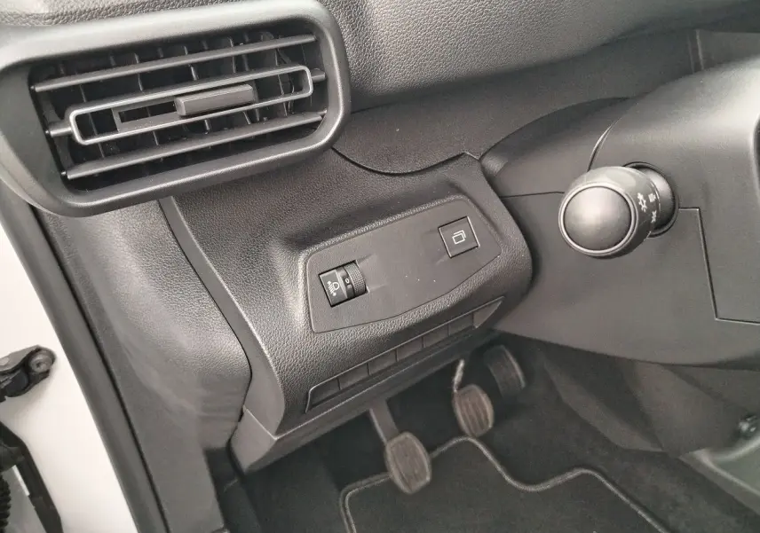 Détail intérieur côté gauche du tableau de bord du Peugeot Partner Fourgon blanc, avec commandes et pédales visibles.