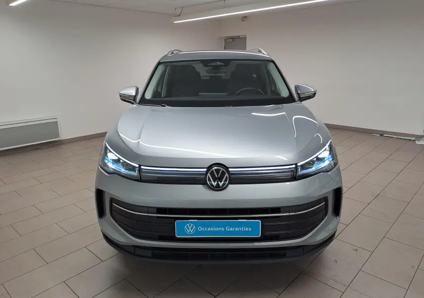 Vue frontale du Volkswagen Tiguan 2.0 TDI 150 DSG7 VW Edition en argent Dolomite avec phares LED allumés dans un showroom.