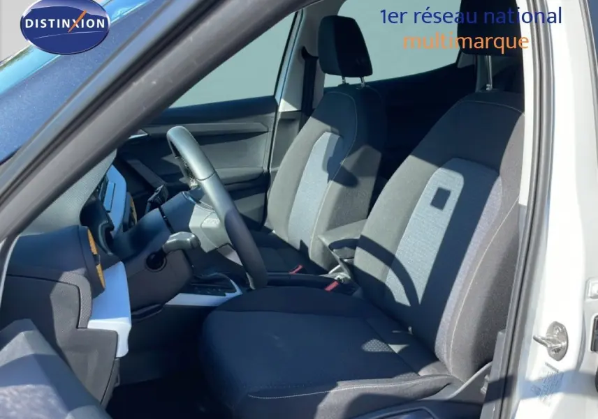 Vue intérieure côté conducteur du SEAT Arona blanc 2025, sièges tissu noir et gris avec volant cuir multifonction.
