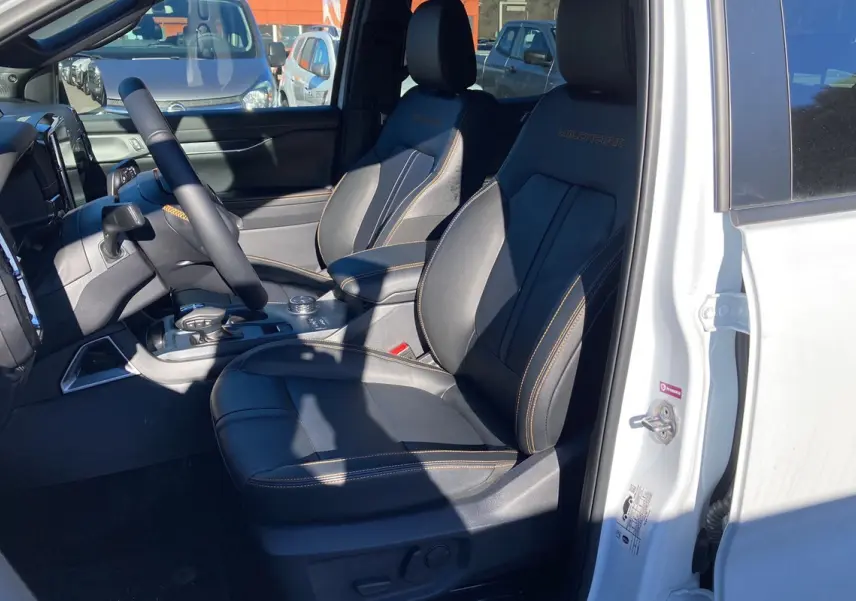 Vue intérieure côté conducteur du Ford Ranger blanc glacier 2026, sièges cuir noirs avec surpiqûres orange Wildtrak.