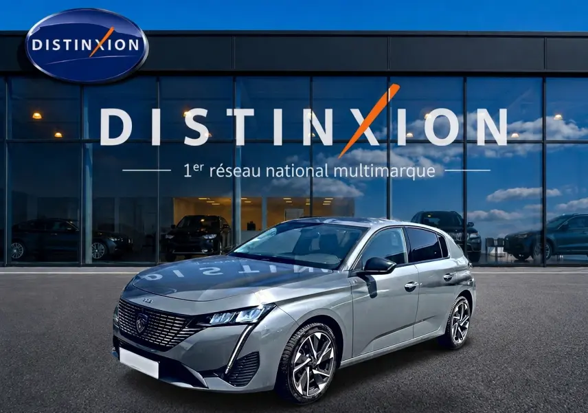Peugeot 308 gris vue 3/4 avant droit, avec calandre distinctive et jantes alliage modernes, devant showroom Distinxion.