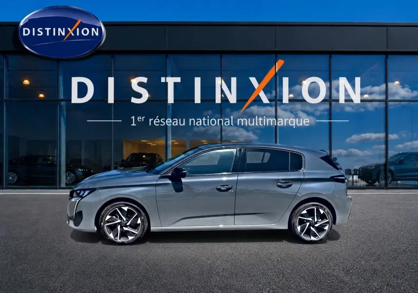 Profil côté gauche d'une Peugeot 308 gris métallisé 2025 avec jantes alliage modernes, devant une vitrine Distinxion.