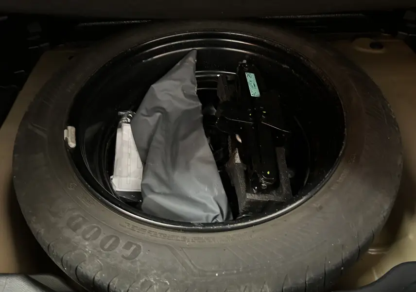 Roue de secours Goodyear avec outillage et housse grise dans le coffre d'une Citroën C4 PureTech 100 Feel orange.