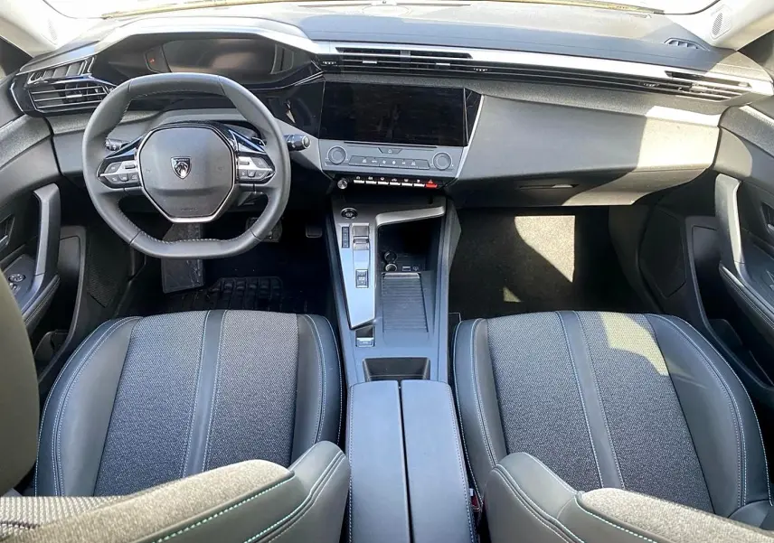 Intérieur de la Peugeot 308 2025 vu de face, montrant le tableau de bord noir et les sièges gris avec surpiqûres.