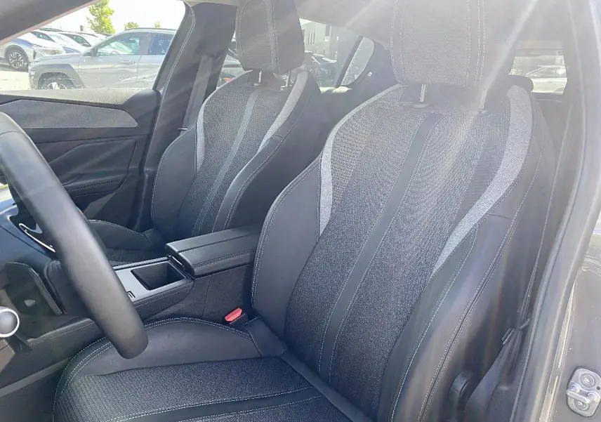 Intérieur de la Peugeot 308 2025, vue sur les sièges avant en tissu gris avec surpiqûres blanches et accoudoir central.