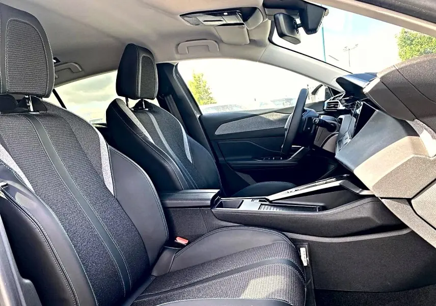 Vue intérieure côté droit de la Peugeot 308 2025, sièges tissu noir avec surpiqûres et console centrale moderne.