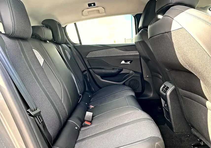 Vue intérieure côté droit montrant la banquette arrière noire avec surpiqûres blanches et les dossiers avant du Peugeot 308 gris.